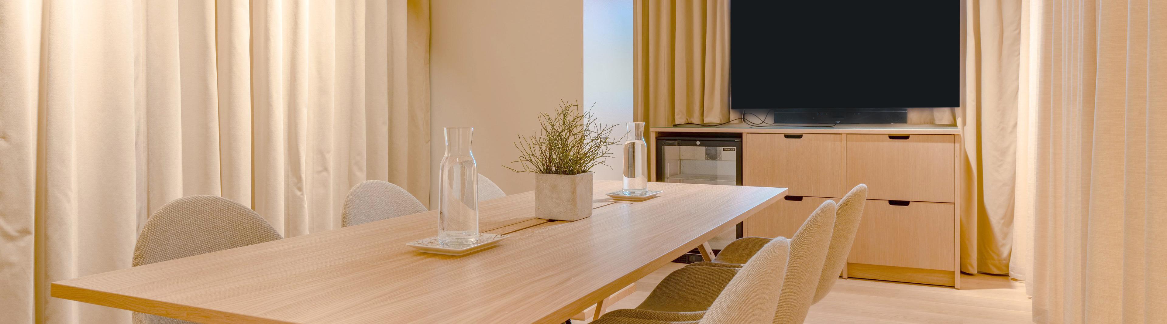 A group of people standing around a table with a fruit arrangement. Background shows stylishly furnished room with wooden flooring and comfortable chairs.